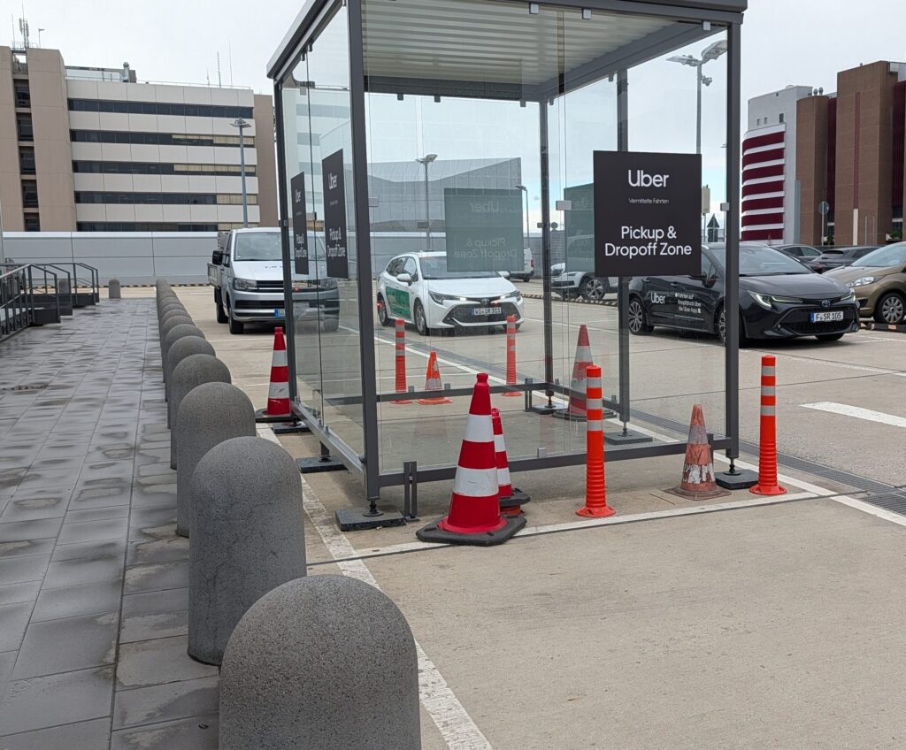 Glass-enclosed Uber waiting shelter at Frankfurt Airport Terminal 1 — covered and weather-protected